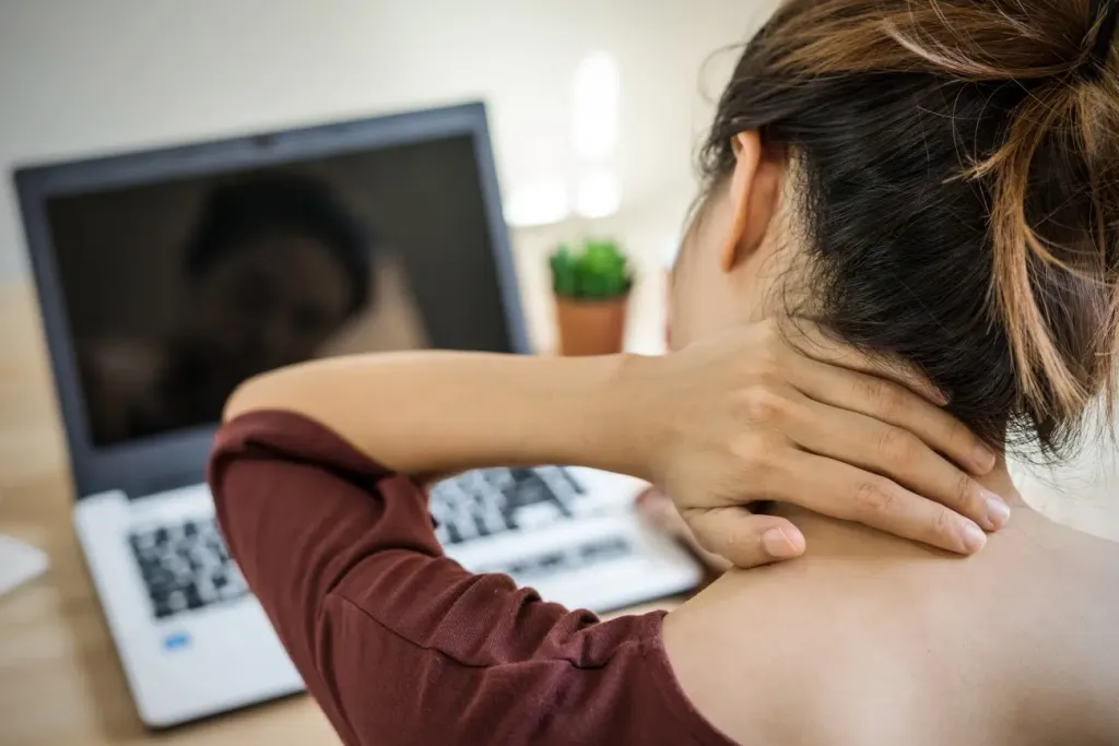 Woman at a laptop holding her neck — typical postural shoulder and neck tension pattern