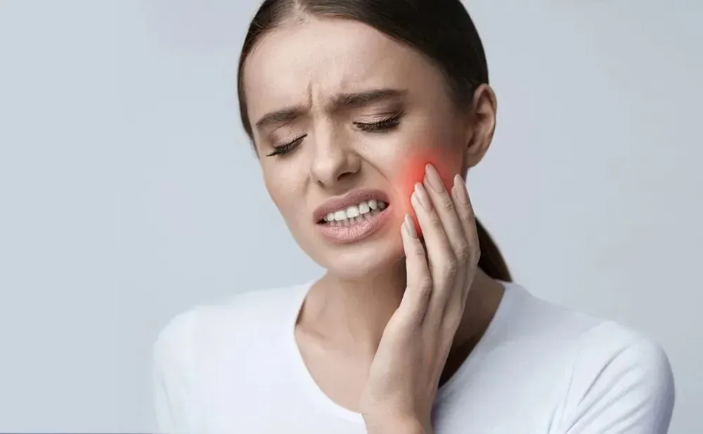 Person holding their jaw with discomfort, indicating TMJ dysfunction