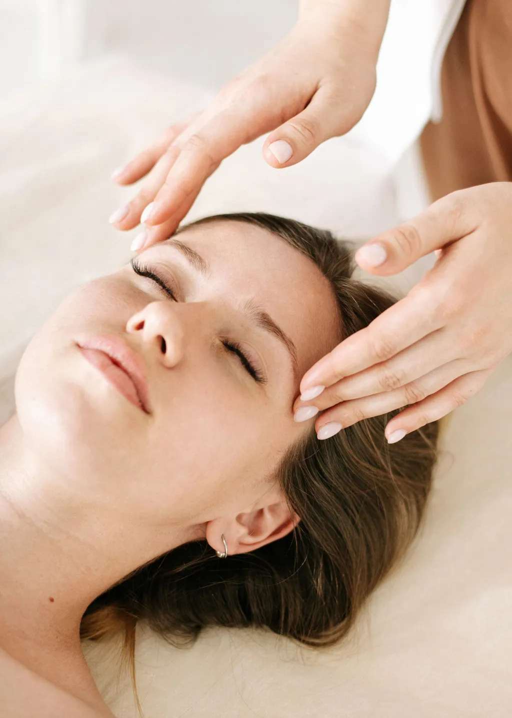 Practitioner’s hands gently placed on a patient’s temples and forehead during a craniosacral therapy session