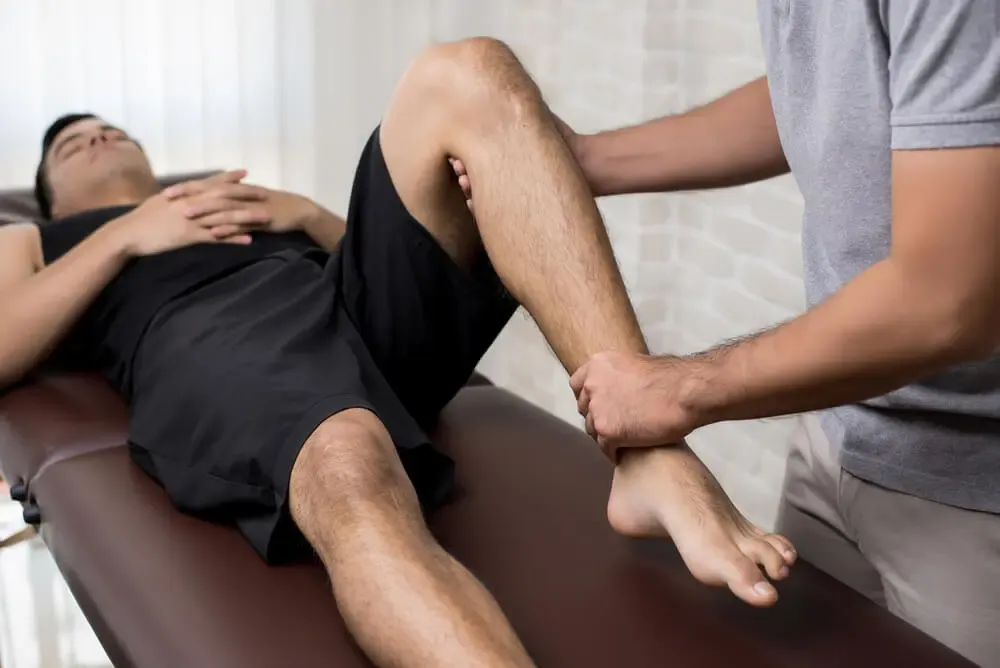 Registered massage therapist using both hands to mobilize a patient's lower leg on a treatment table